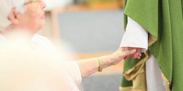 Der Geistliche hält die Hand einer älteren Dame.