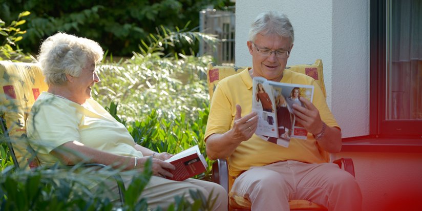 Eine Bewohnerin und ein älterer Herr lesen gemeinsam im Garten.