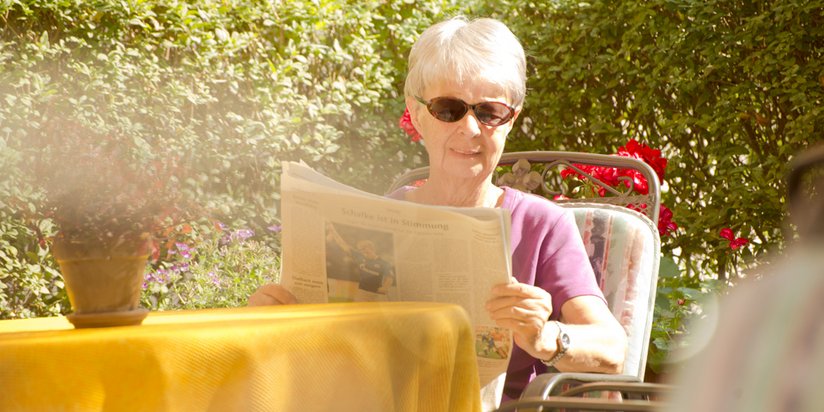 Eine Bewohnerin liest die Zeitung und genießt die Sonne im Garten.