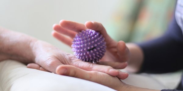 Eine Betreuerin massiert die Hand einer Bewohnerin mit einem Massageball.