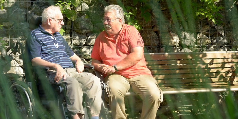 Zwei Senioren plaudern gemeinsam auf einer Parkbank.