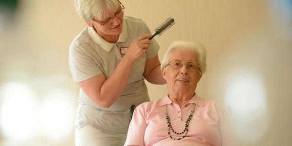 Eine Friseurin richtet die Haare einer Bewohnerin.