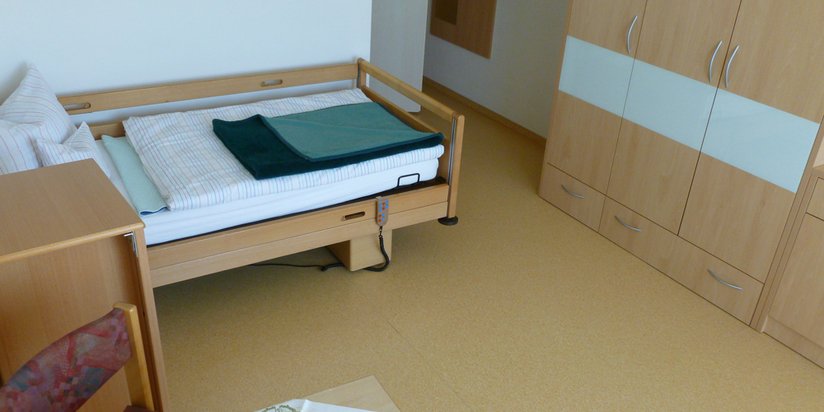 Einblick in ein Bewohnerzimmer inklusive Bett mit Pflegefunktionen.