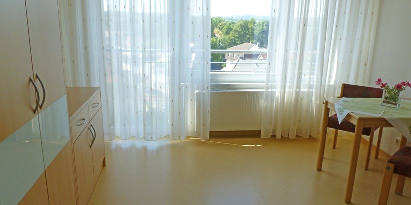 Bewohnerzimmer mit Sitzgelegenheit, Schrank und Kommode.